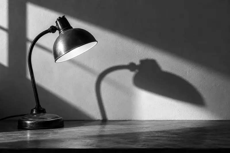 Lampa biurkowa rzucająca ostry cień na pustą ścianę.