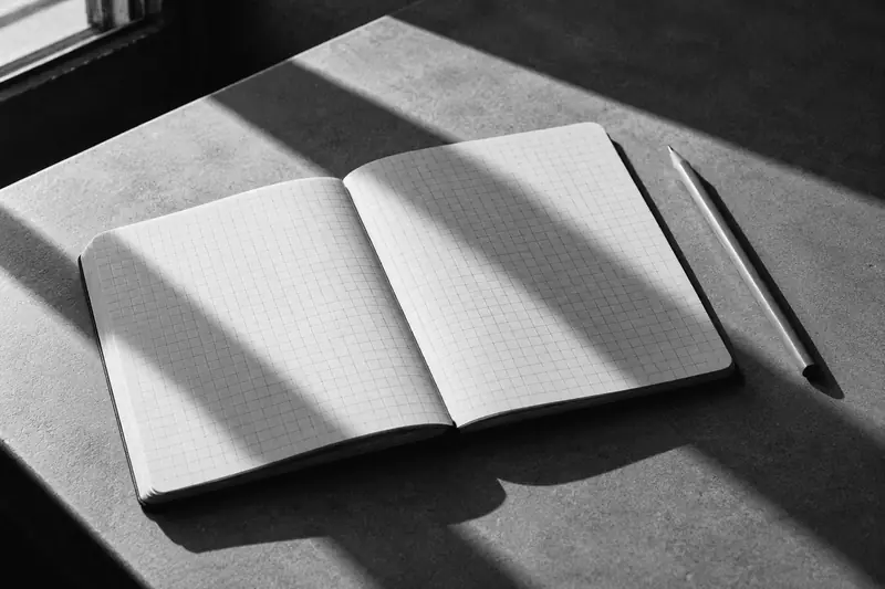 Otwarty notes w kratkę i ołówek na blacie.